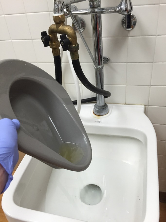 pouring the contents of a bedpan into a sink